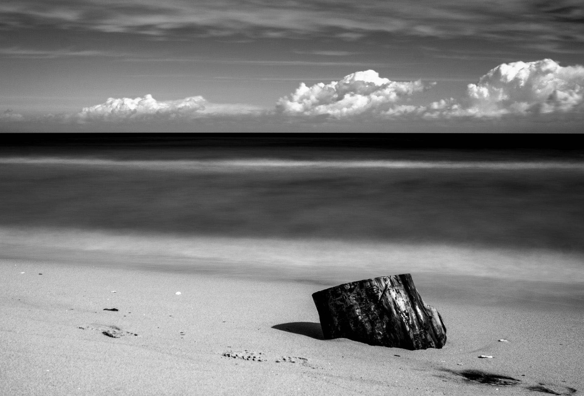 Tronco sulla spiaggio e nuvole, black and white long exposure photography